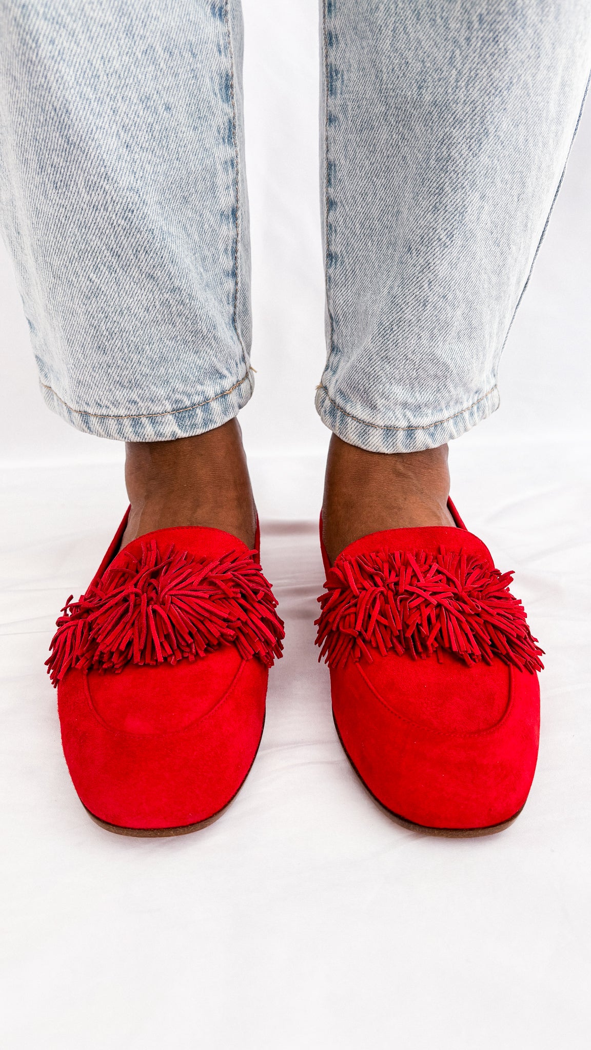 Close-up on-foot view from the front of the Aquazzura Wild Thing red suede loafers, showcasing the full fringe texture.
