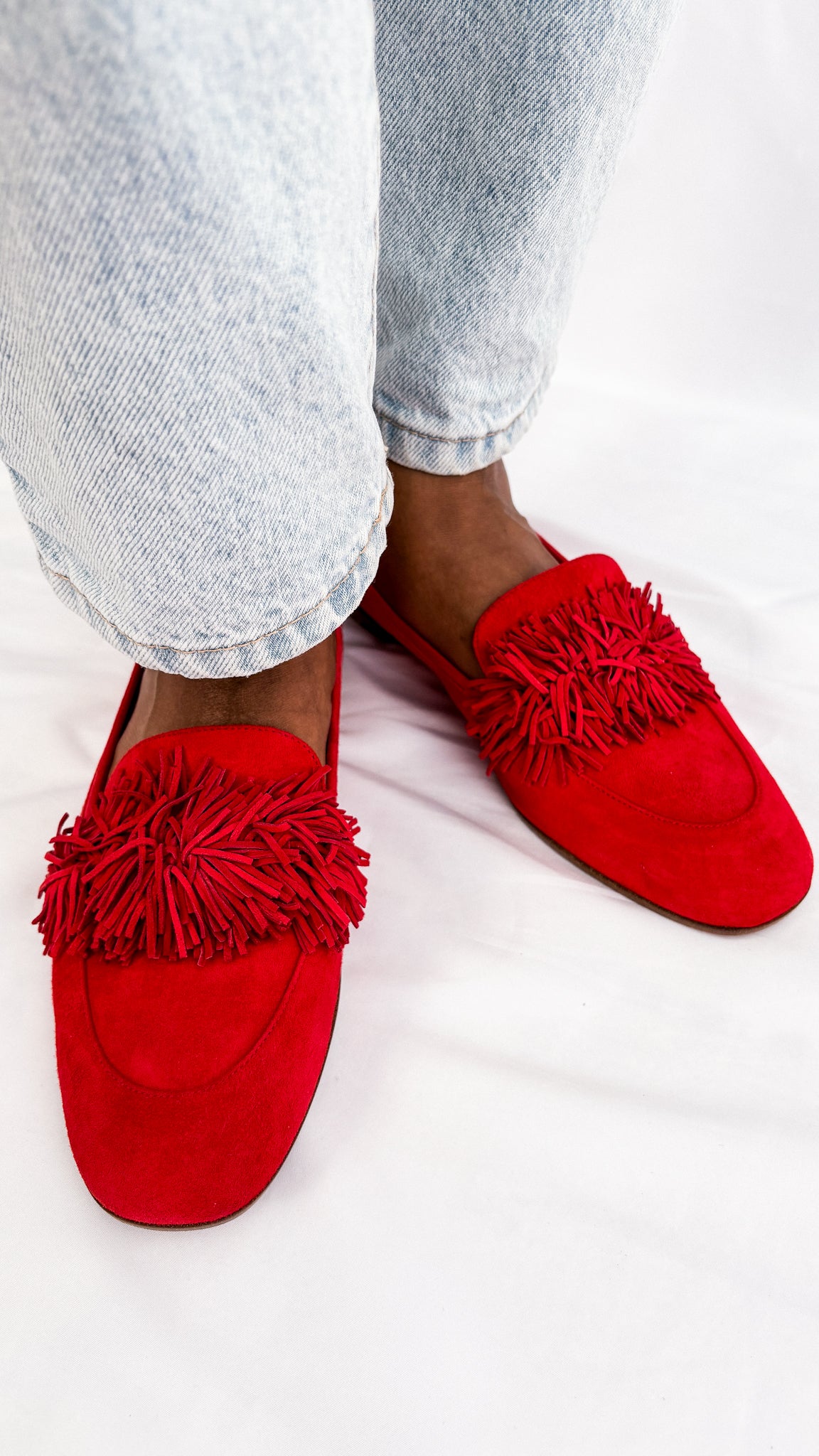 On-foot wearing view of a pair of red suede Aquazzura Wild Thing loafer flats styled with light wash denim jeans.