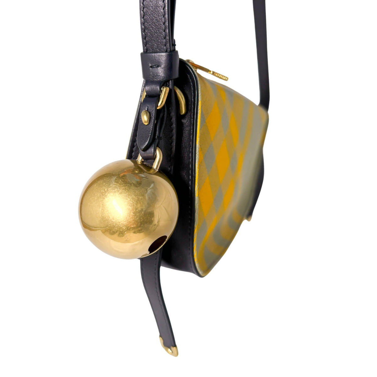 Detailed close-up of the hanging gold-tone bell charm and black leather trim on the Burberry Shield shoulder bag.