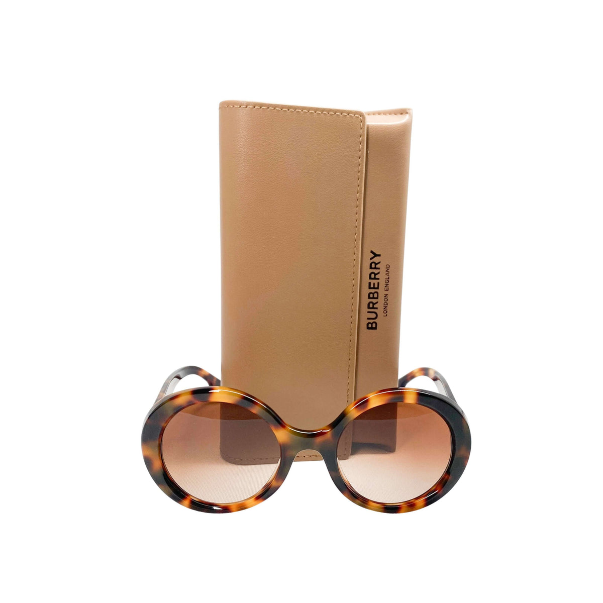 Burberry round tortoiseshell sunglasses displayed resting in front of the included tan hard leather case.