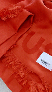 Folded vermillion red Burberry Monogram scarf displaying the interlocking TB motif pattern texture.