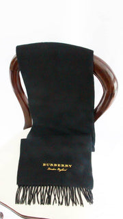 Burberry black 100% cashmere scarf with gold embroidered logo and fringe trim draped over a display stand.