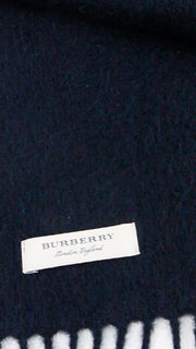 Close-up view of the white woven Burberry brand label stitched onto the black cashmere scarf.