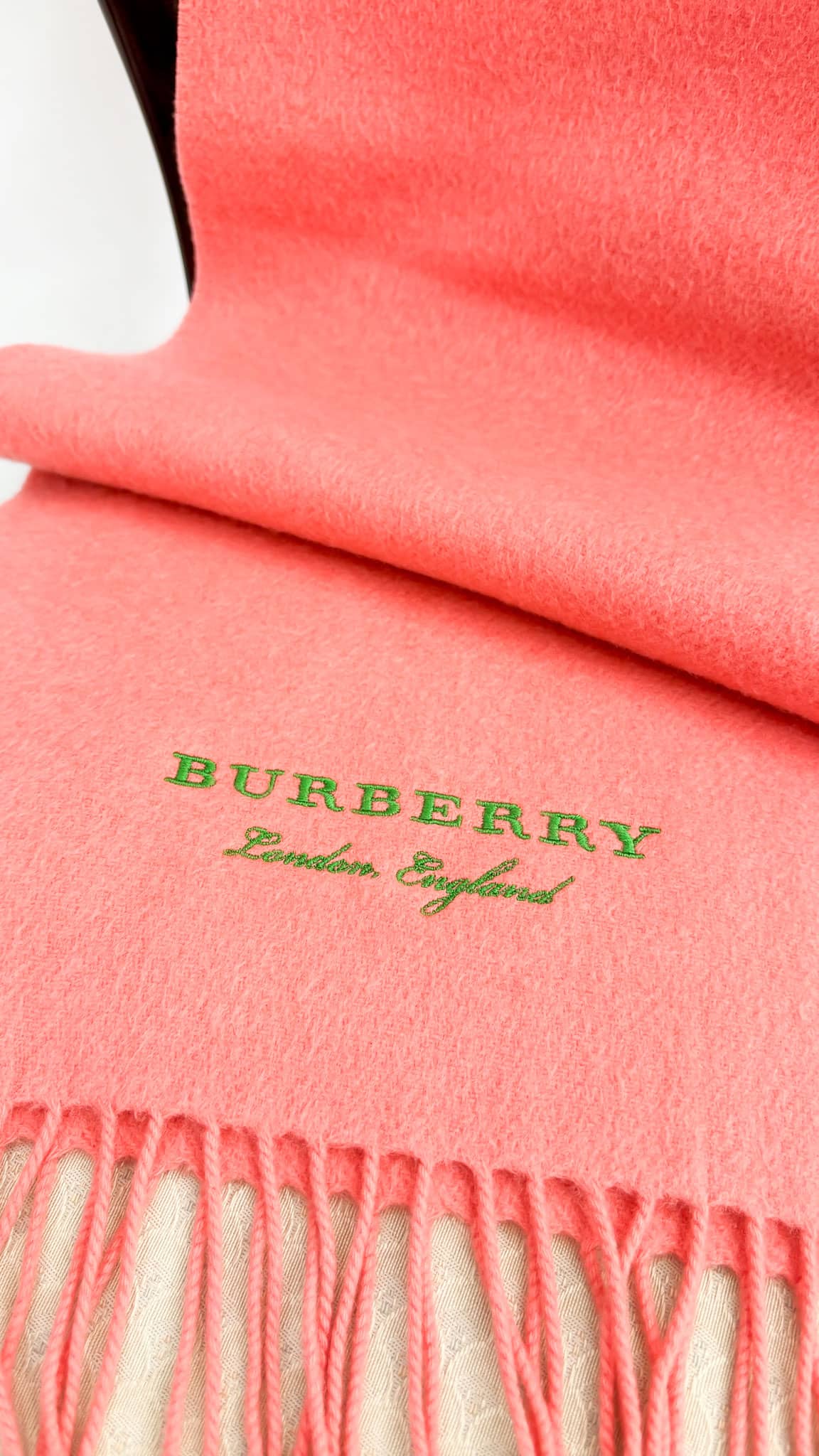 Detailed view of the coral pink Burberry cashmere scarf showcasing the tonal embroidered Burberry logo and soft woven texture.