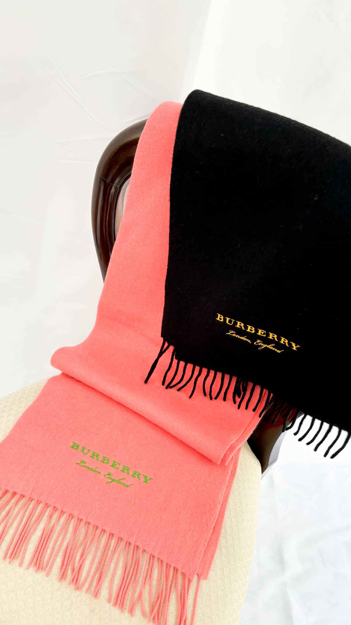Profile view of the coral pink Burberry cashmere scarf draped over a black neck mannequin with attached brand tag.