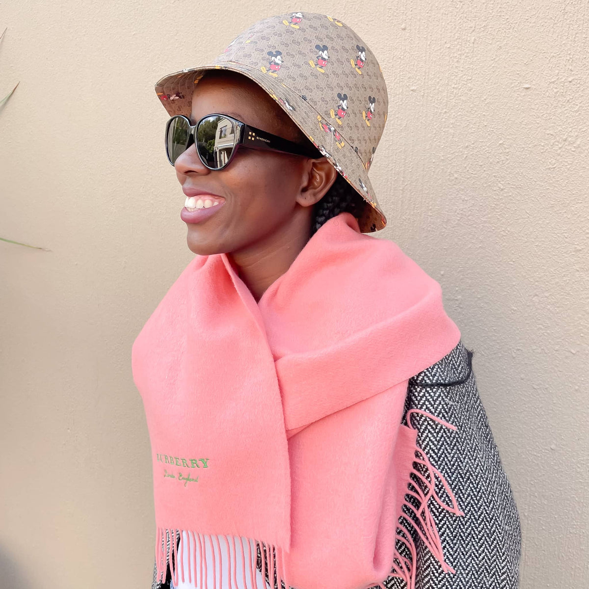 Model wearing the coral pink Burberry cashmere scarf draped over shoulders outdoors with sunglasses.