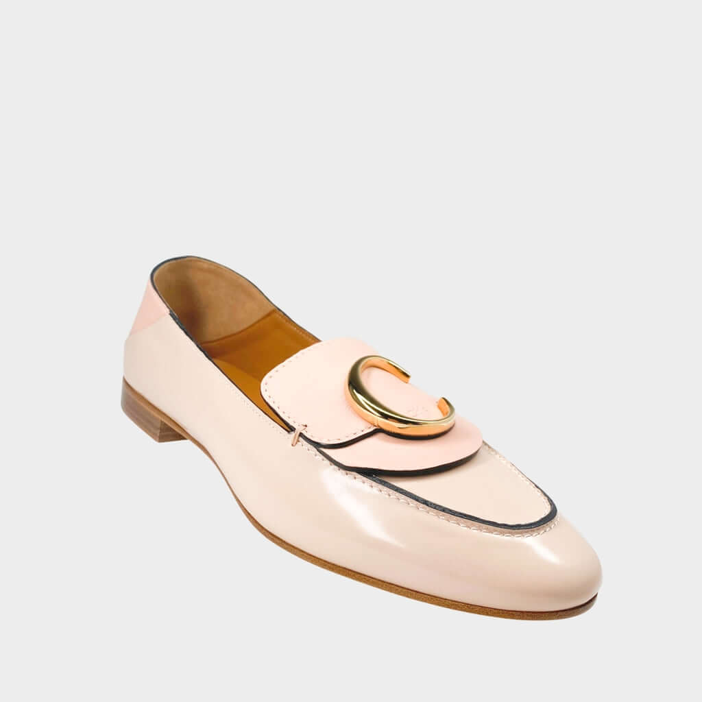 Side profile close-up of a Chloé C loafer in pink patent leather, showcasing the prominent gold-toned C initial logo on the strap and the stacked flat heel.