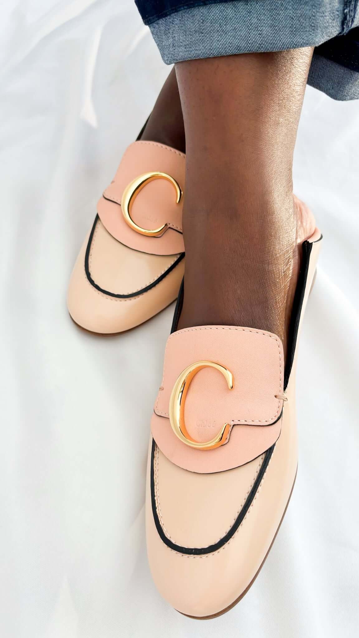 On-foot wearing view of a pair of pink patent leather Chloé C loafers styled with blue jeans, highlighting the round toe design.