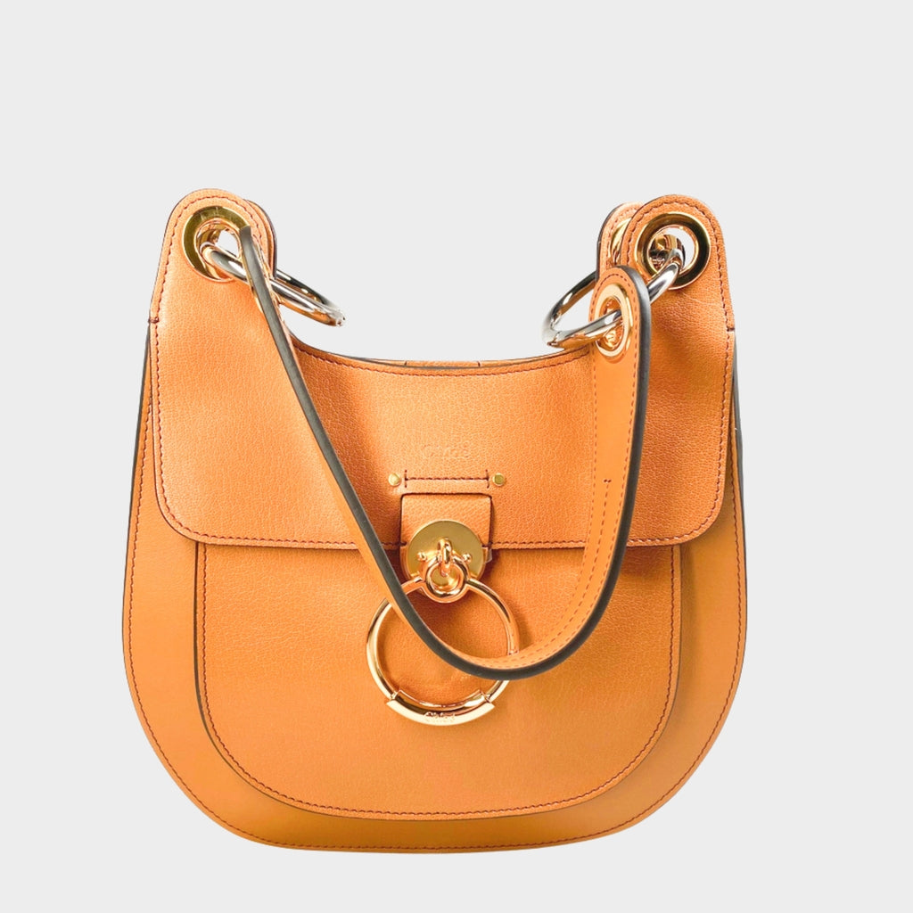 Front close-up view of the Chloé Tess shoulder bag in orange-brown calfskin leather, highlighting the signature gold-toned ring hardware.