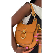 On-body view of a model carrying the orange-brown leather Chloé Tess bag by its short top handle, styled with a cream sleeveless top.
