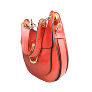 Right side three-quarter profile of the red Chloé Tess leather bag, highlighting its curved saddle silhouette and structured side panel detailing.
