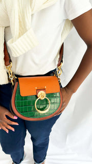 Front perspective wearing shot of a model holding the brown and green embossed leather Chloé Tess handbag by its short top handle strap.