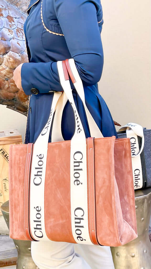 Rear three-quarter view of a model carrying the Chloé Woody brown suede medium tote bag, styled with a classic blue button-down shirt.