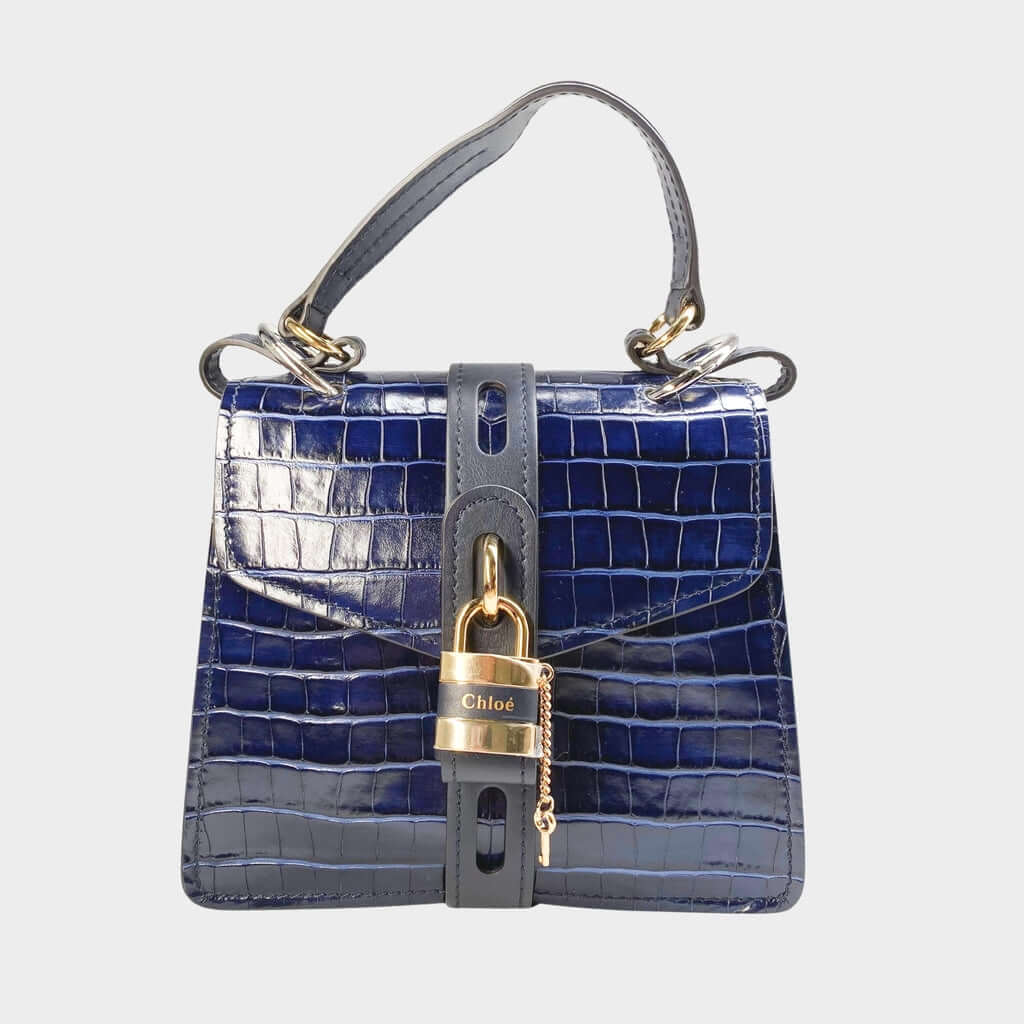 Front close-up view of the Chloé Aby Day Shoulder Bag in navy blue croc-embossed calfskin leather, showcasing the gold-toned heritage padlock.