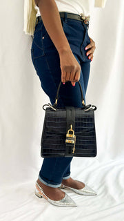 On-foot wearing view of a model carrying the Chloé Aby Day navy blue embossed leather handbag by its top handle, paired with dark denim jeans.