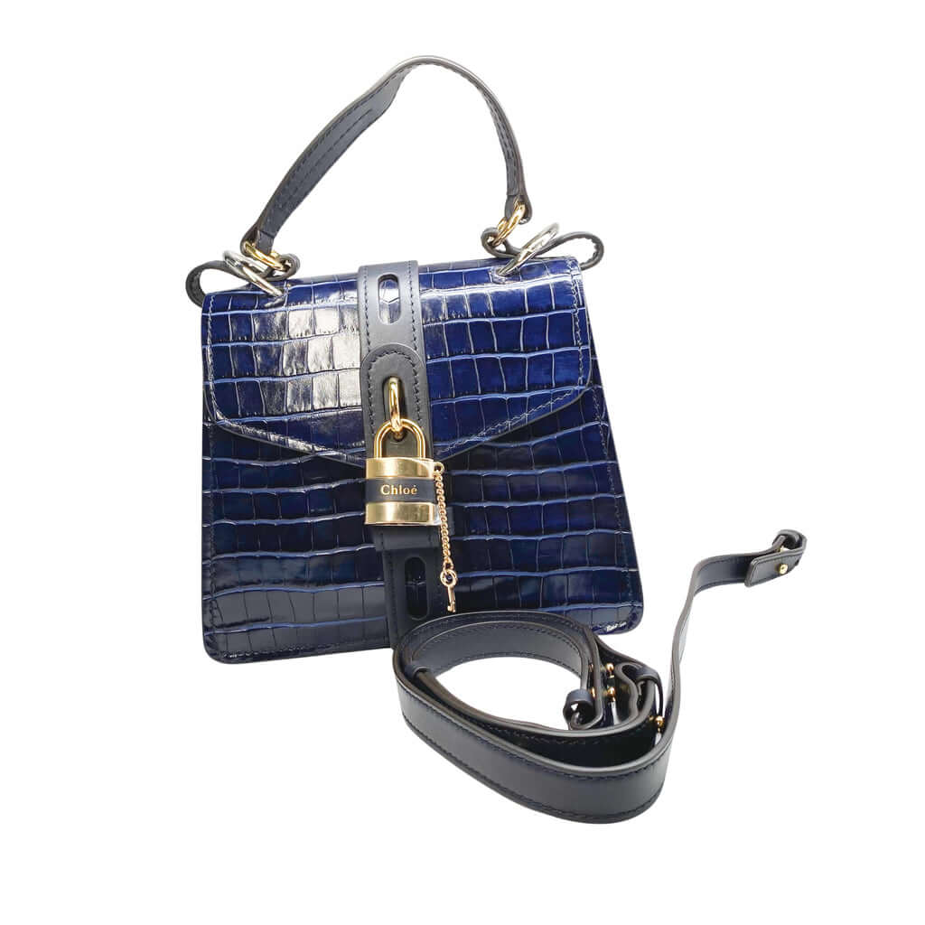 Front studio view of the Chloé Aby Day navy blue croc-embossed shoulder bag against a white background, featuring the detachable leather crossbody strap.