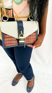 Close-up on-body view of a model holding the tri-color Chloé Aby Day Chain bag, highlighting the white and blue leather panel details.