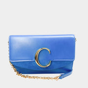 Front close-up view of the Chloé C Crossbody Bag in blue calf leather, showcasing the prominent gold-toned C logo plaque on the foldover top.
