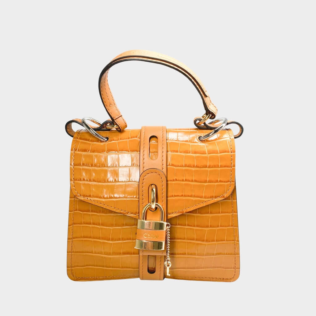Front close-up view of the Chloé Aby Day Shoulder Bag in Ocre brown croc-embossed calfskin leather, showcasing the gold-toned heritage padlock.