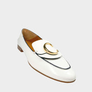 Side profile close-up of a Chloé C loafer in white patent leather, showcasing the prominent gold-toned C initial logo on the strap and the stacked flat heel.