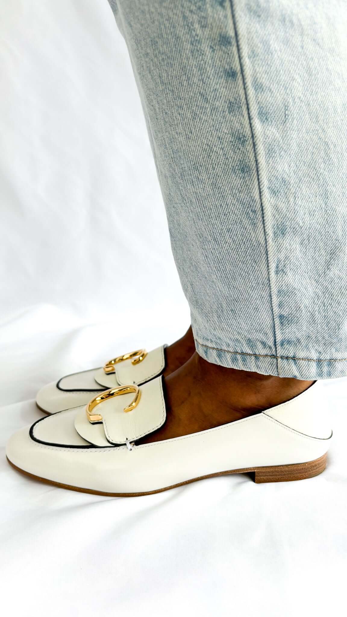 Side angle on-foot view of the Chloé C white patent leather loafers, showing the classic slip-on flat silhouette.