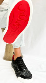 Close-up of a model lifting a foot to showcase the signature bright red rubber outsole of the Christian Louboutin Aurelien sneaker