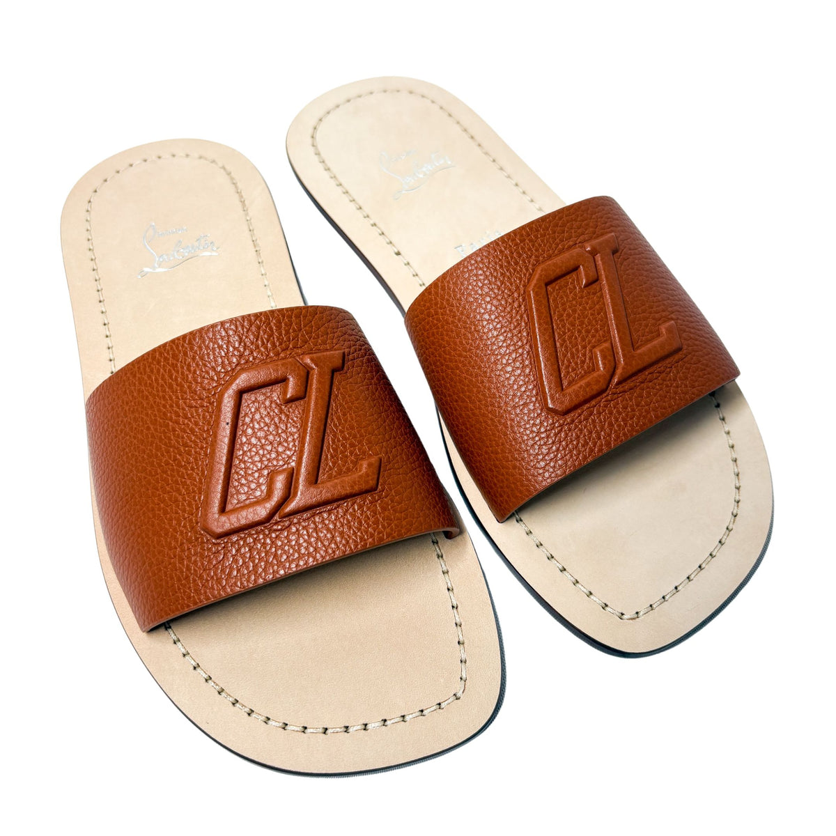 Top-down parallel studio shot of a pair of Christian Louboutin Varsicool brown leather slide sandals side-by-side.