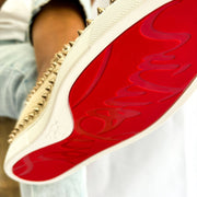 Close-up on-foot view of a model lifting a pink Christian Louboutin studded espadrille to display the iconic scarlet red rubber outsole.