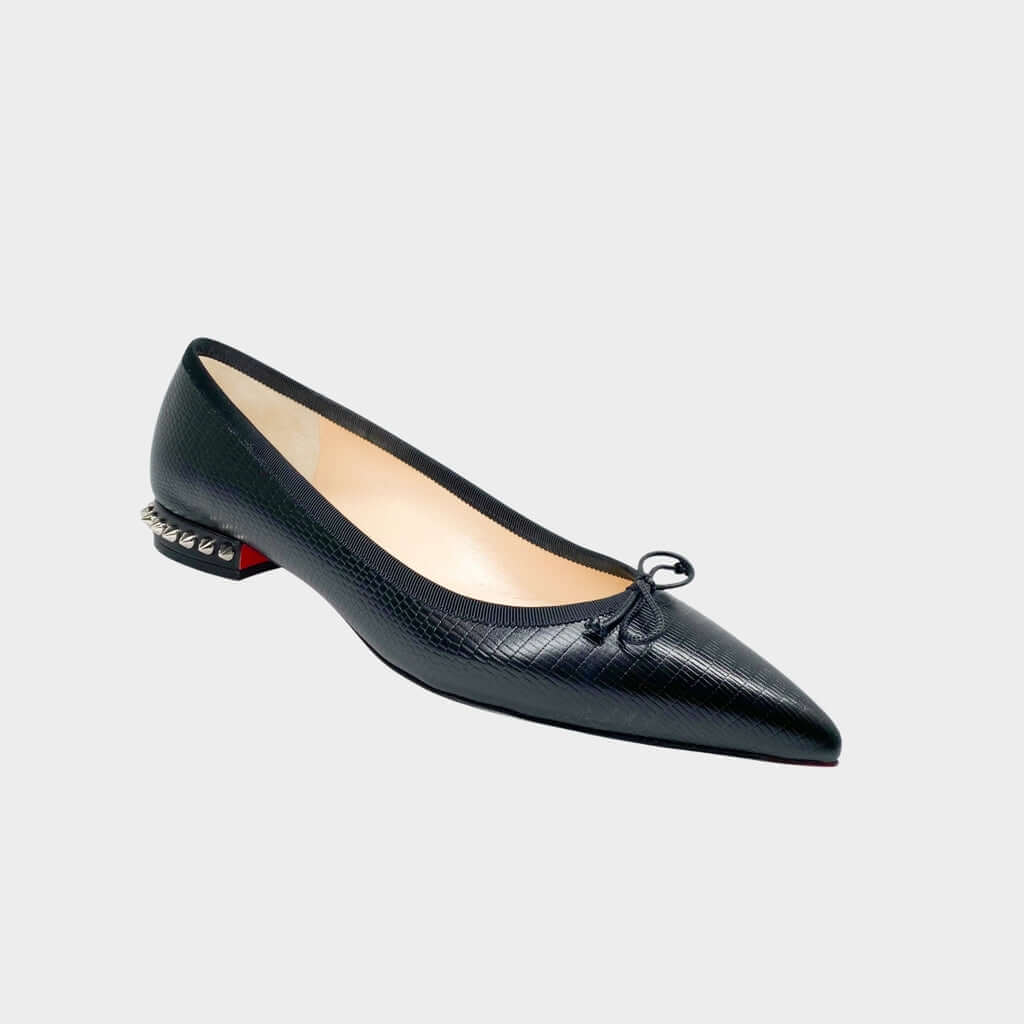 Side profile close-up of a Christian Louboutin Hall ballet flat in black smooth leather, showcasing the pointed toe and small stacked heel adorned with silver spikes.