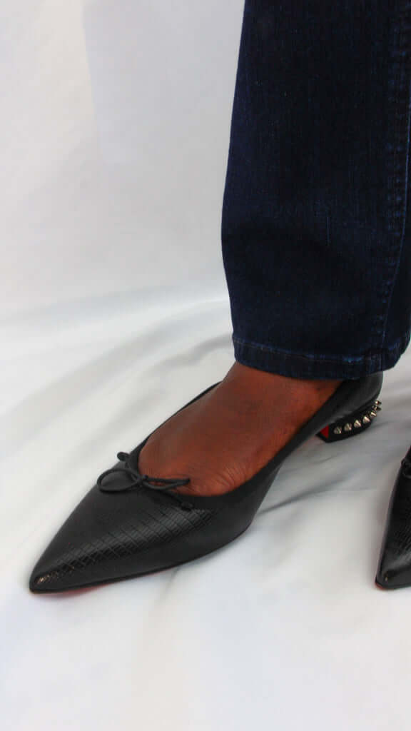 Top-down on-foot wearing view of a model in the black leather Christian Louboutin Hall pointed-toe flats.