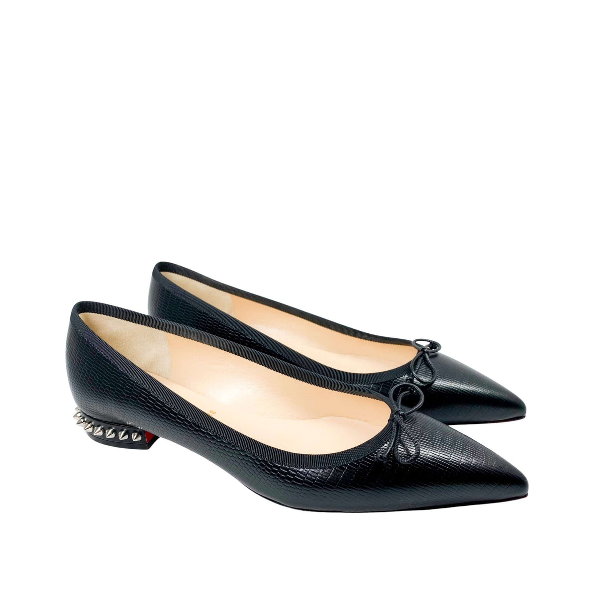 Side angle studio shot of a pair of black leather Christian Louboutin Hall flats, focusing on the spiked heels and crisp beige leather lining.