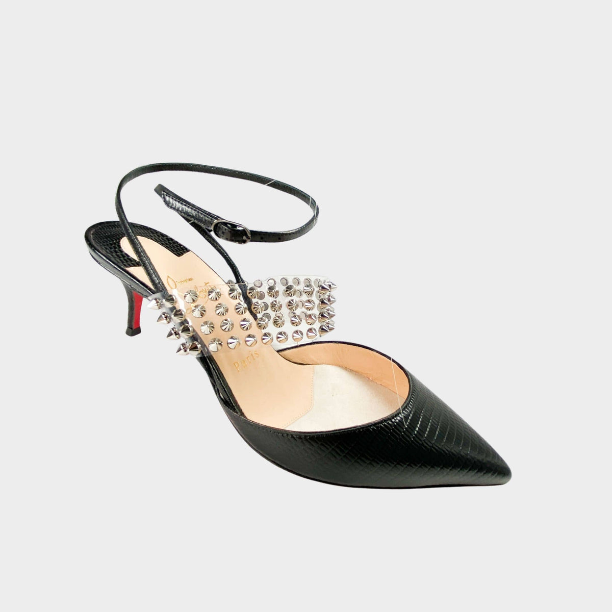 Side profile close-up of a Christian Louboutin Levita 55 pump in black embossed leather, showcasing the transparent PVC upper, pyramid-studded ankle strap, and kitten heel.