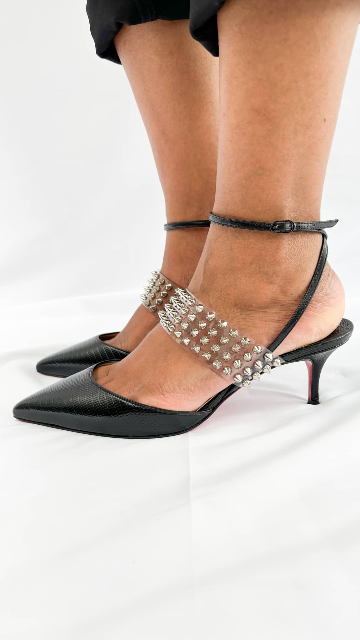 Side profile wearing view of the Christian Louboutin Levita 55 black studded pumps, styled with cropped black trousers.