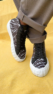 On-foot view of model wearing Fendi FF Vertigo high-top sneakers with beige trousers.