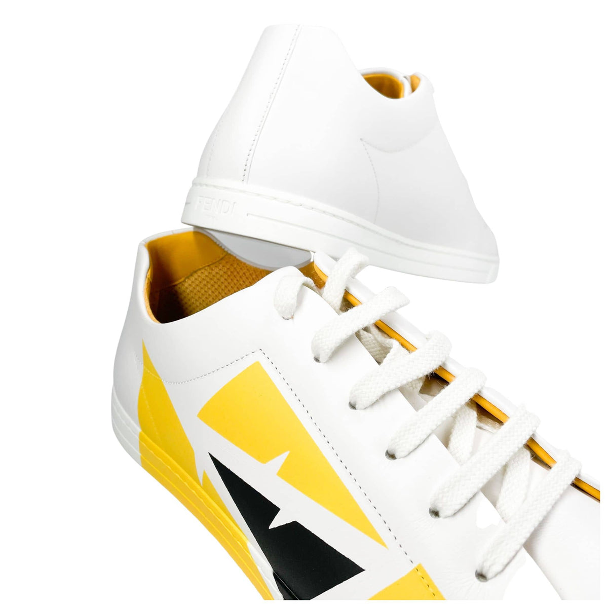 Low-angle perspective view of Fendi Bag Bugs white leather sneakers highlighting front yellow motif.