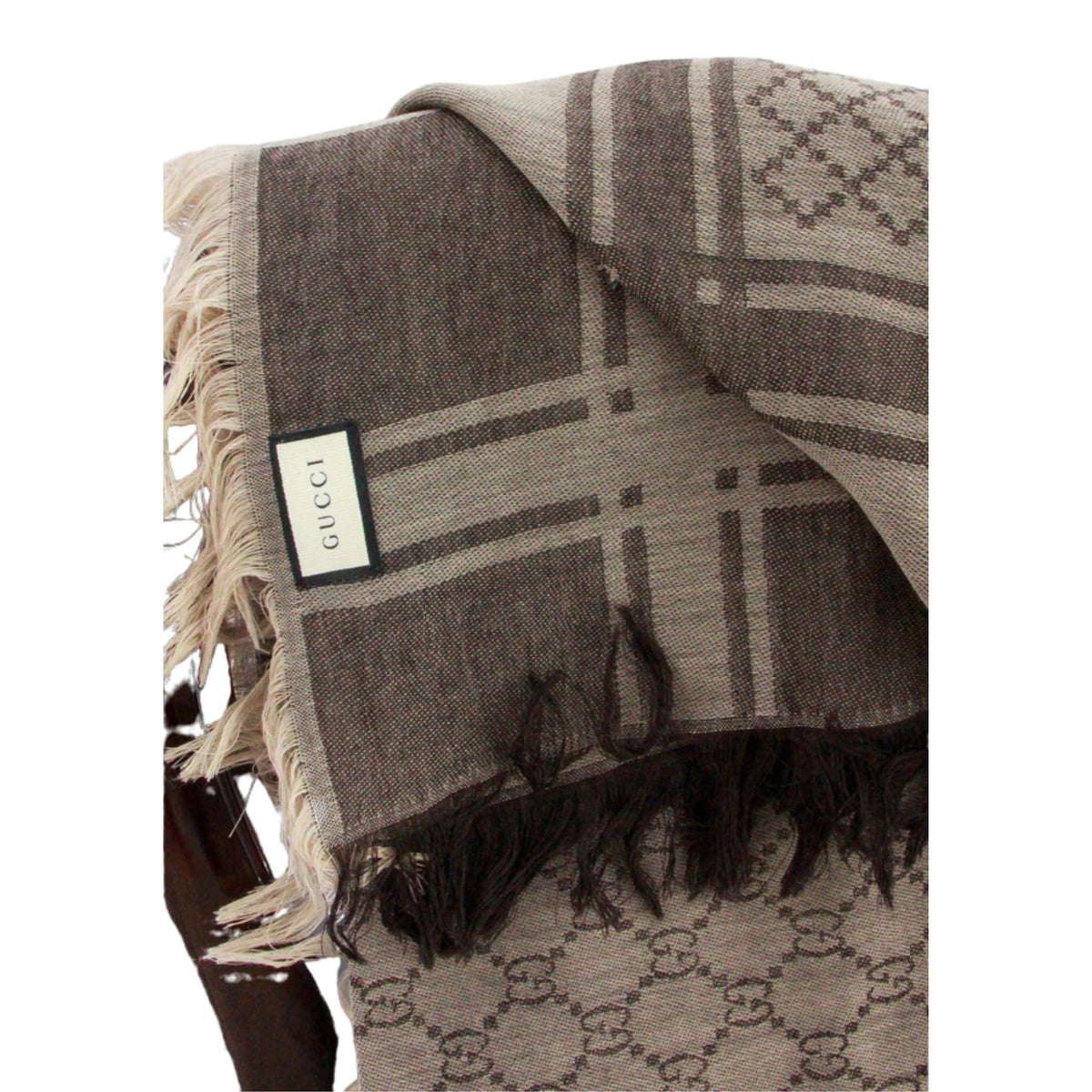 Close-up view of brown Gucci GG monogram scarf displaying woven fabric texture, fringe border, and care tag.
