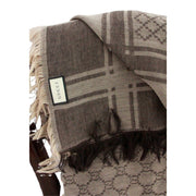 Close-up view of brown Gucci GG monogram scarf displaying woven fabric texture, fringe border, and care tag.