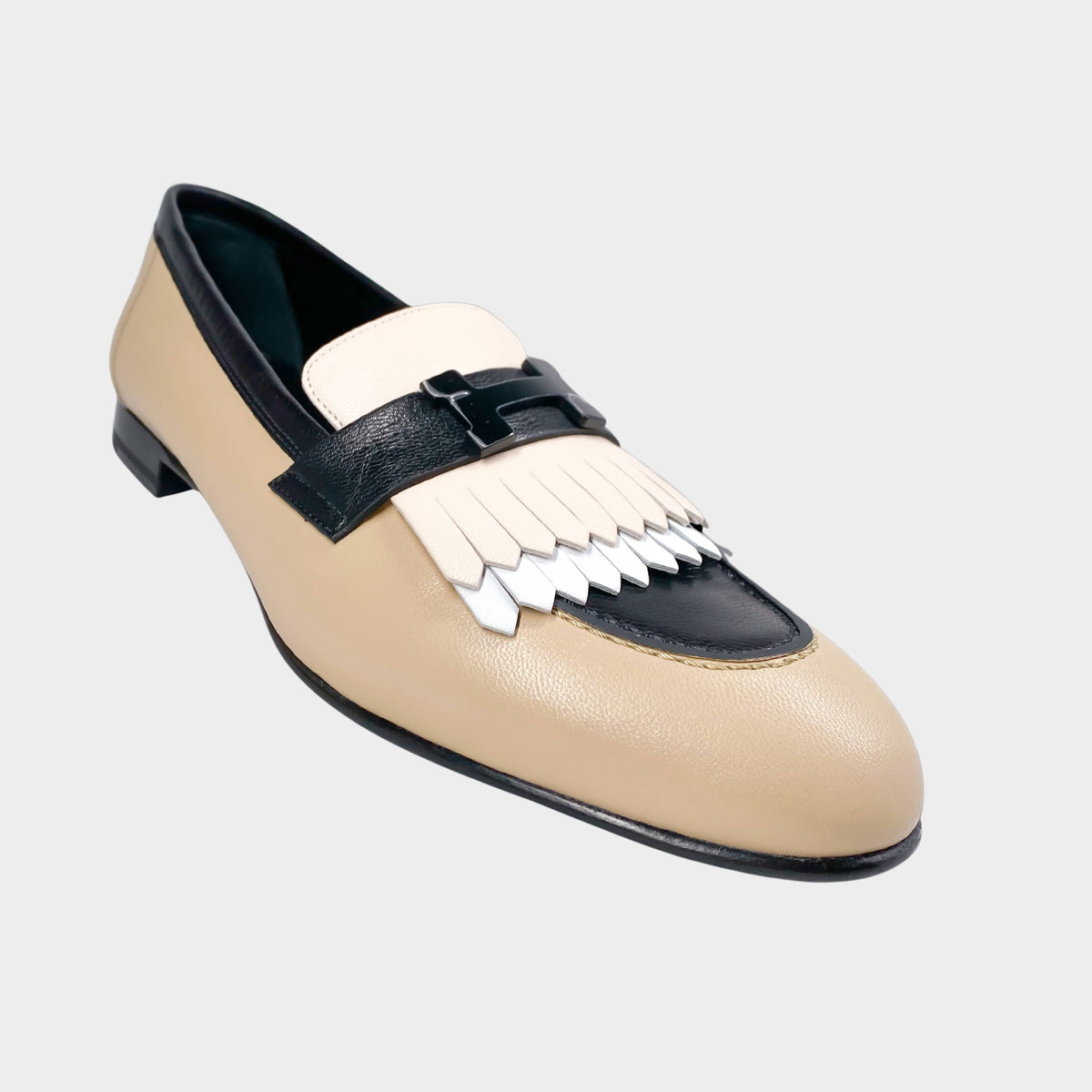 A detailed profile perspective of the multi-toned Hermès Royal loafer, emphasizing the contrast between the smooth cream calfskin body and the layered white fringed kiltie detail on the vamp.