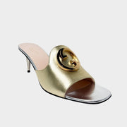 Side profile view of a Gucci Blondie mule sandal in metallic gold leather, featuring a prominent circular gold interlocking G logo and a sleek silver stiletto heel.