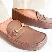Three-quarter angle view of Gucci brown leather men's horsebit slip-on shoe highlighting horsebit hardware.