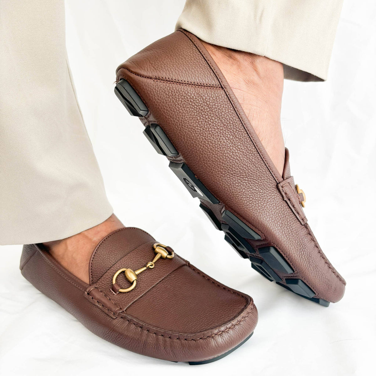 On-foot dynamic view of Gucci brown leather Horsebit loafers styled with light beige trousers.