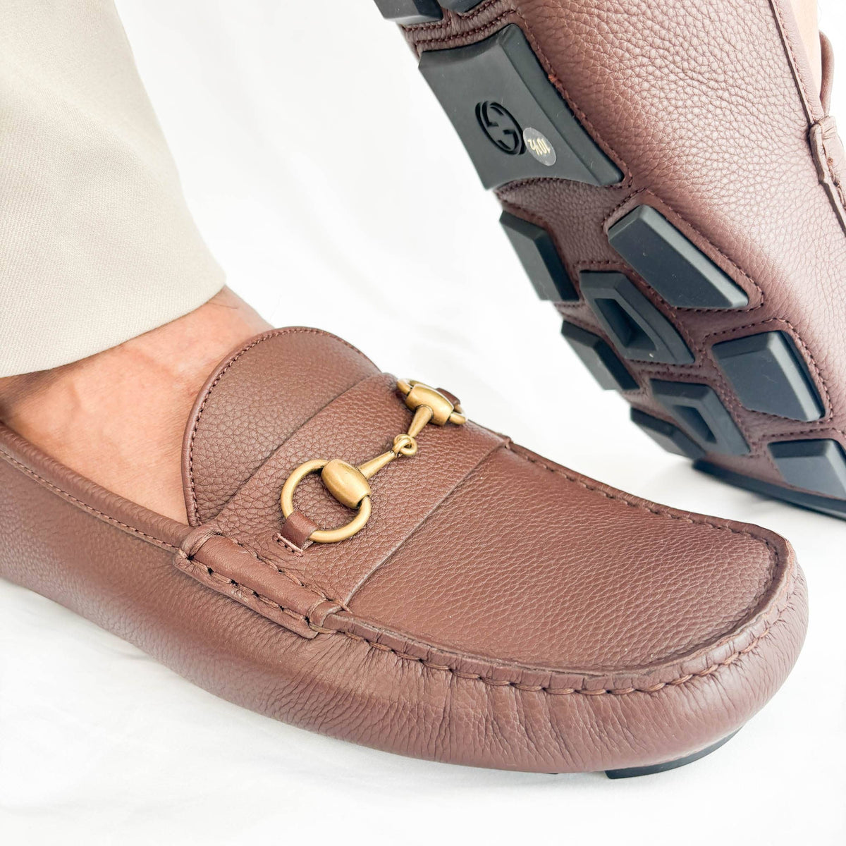 Close-up view of gold-tone horsebit detail on Gucci brown leather driver loafers.