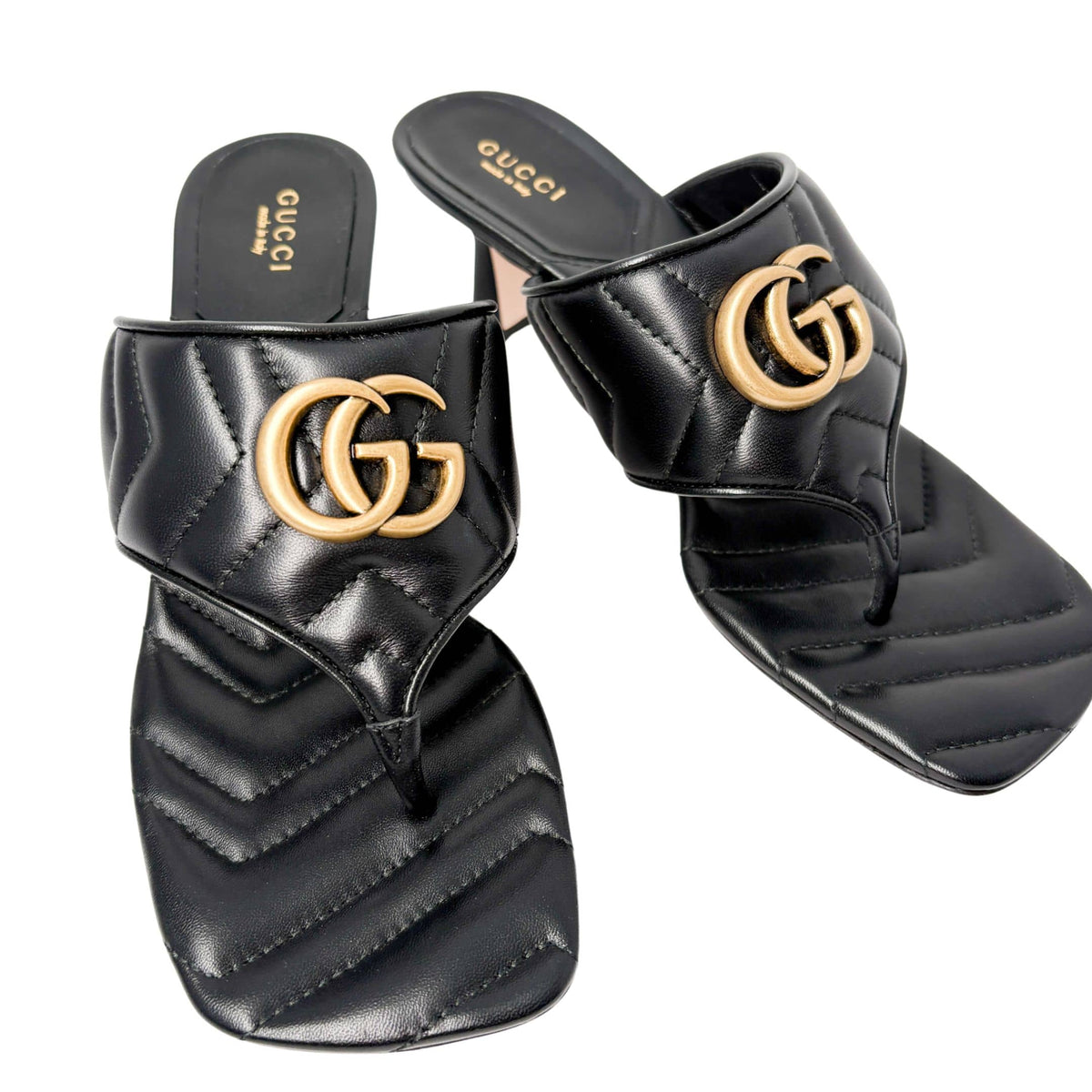 Three-quarter studio perspective of a pair of black Gucci Charlotte thong sandals, showcasing the quilted chevron pattern across the wide strap.