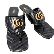 Three-quarter studio perspective of a pair of black Gucci Charlotte thong sandals, showcasing the quilted chevron pattern across the wide strap.