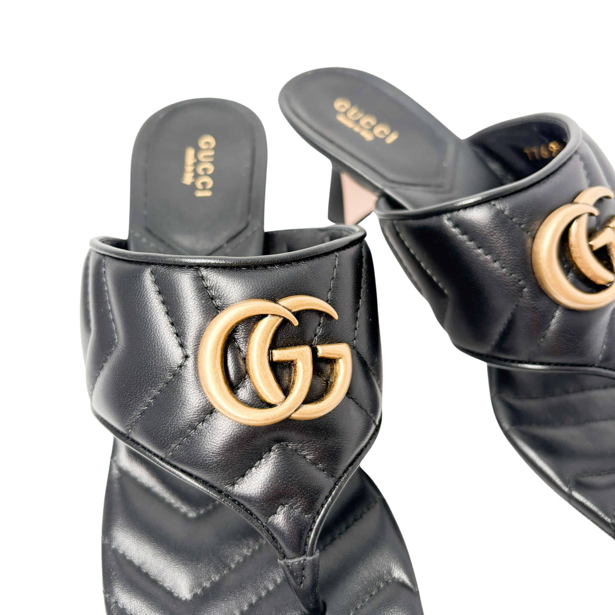 Top-down angled view of a pair of black leather Gucci Charlotte sandals, displaying the sleek T-strap silhouette and gold-tone hardware.