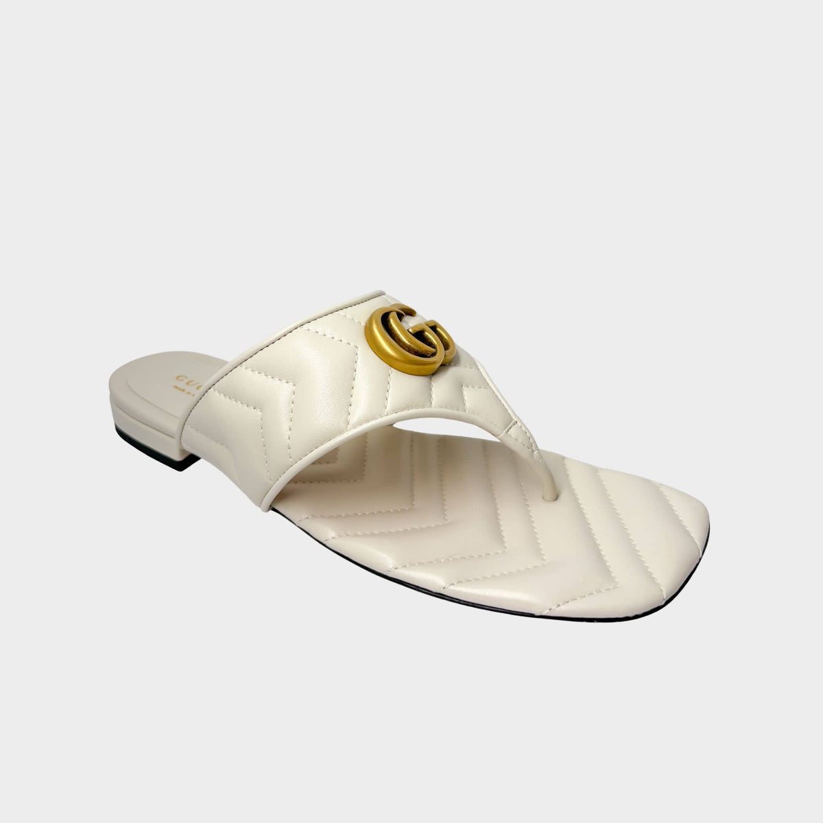 Side profile view of a Gucci Marmont Charlotte thong slide sandal in off-white quilted leather, featuring a prominent gold-toned GG logo.