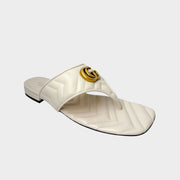 Side profile view of a Gucci Marmont Charlotte thong slide sandal in off-white quilted leather, featuring a prominent gold-toned GG logo.