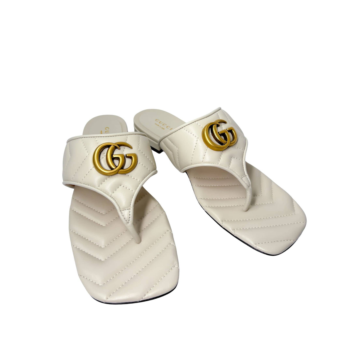 Angled studio arrangement of the white leather Gucci Charlotte thong sandals, displaying the sleek T-strap silhouette.