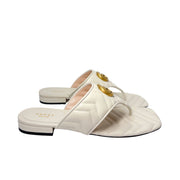 Detailed angle shot focusing on the iconic gold-tone GG Marmont logo attached to the white leather strap of the Gucci Charlotte sandal.