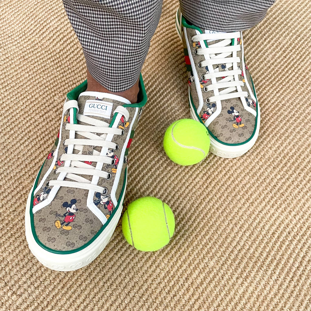 Overhead on-foot shot of Gucci Tennis 1977 Mickey Mouse sneakers on a court with tennis balls.